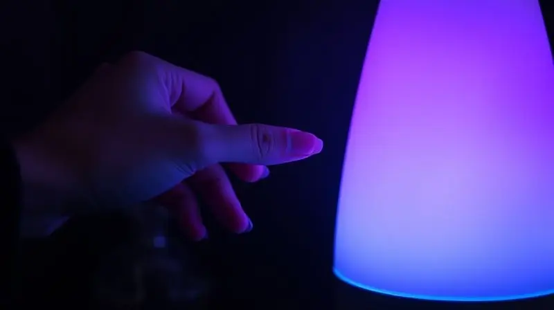 Close-up de um difusor com iluminação LED colorida em um quarto escuro, destacando suas funcionalidades extras e design.