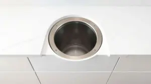 Fotografia profissional de uma lixeira de embutir moderna em inox, instalada numa bancada de cozinha, ilustrando os melhores modelos do mercado.